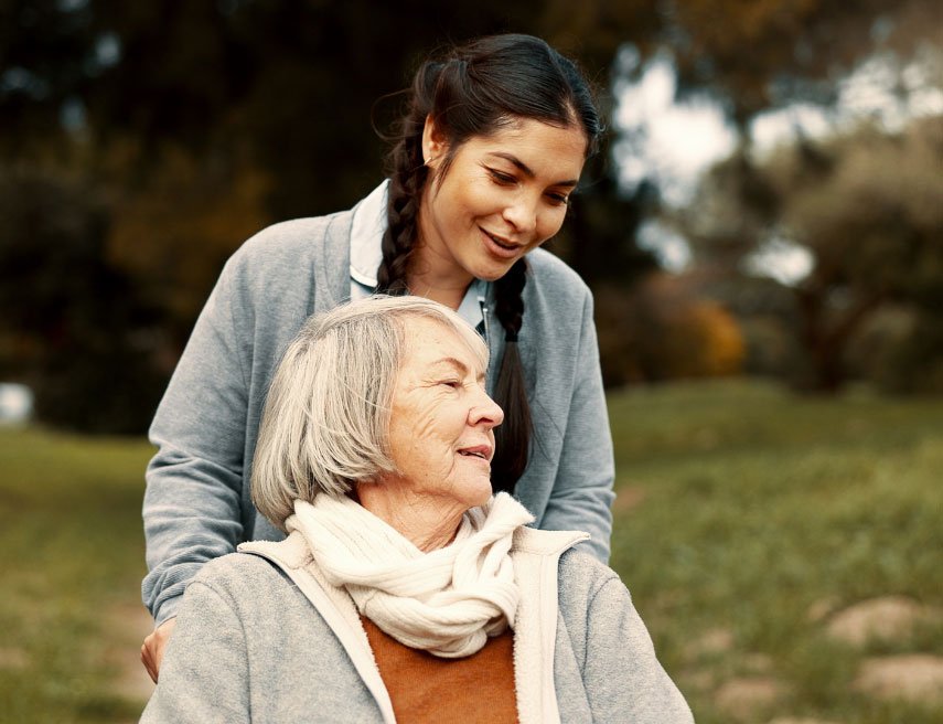 Una mujer cuidadora empuja la silla de ruedas de otra mujer en un parque