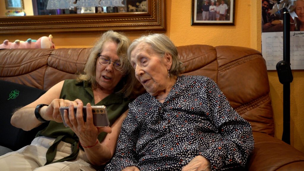 Marisa enseña al Juliana un vídeo en el móvil. Ambas están sentadas en el sofá.