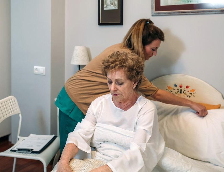 Una mujer cuidadora coloca la almohada para una persona mayor en sus dormitorio.