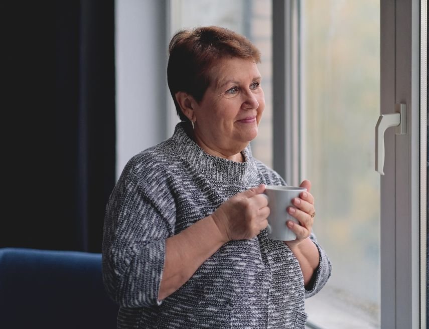 Una mujer mira por la ventana con una taza de café.
