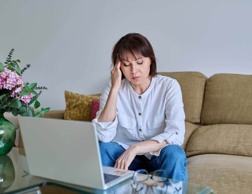 Una mujer, sentada en el sofá frente a un portátil, parece agotada.